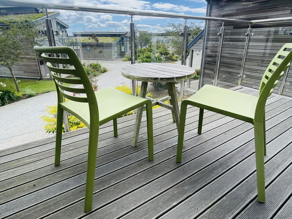 Two green chairs and a wood table on a deck at Una, Lodge 73 Carbis Bay