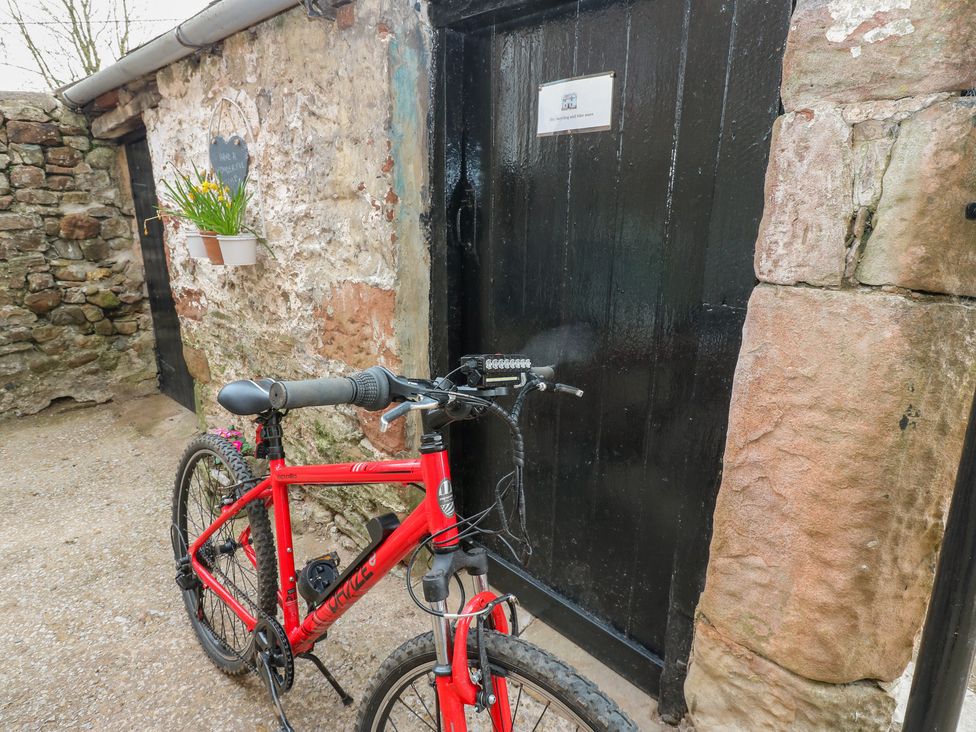 A red bicycle next to a black door and stone wall at 1 Brookside in Warcop