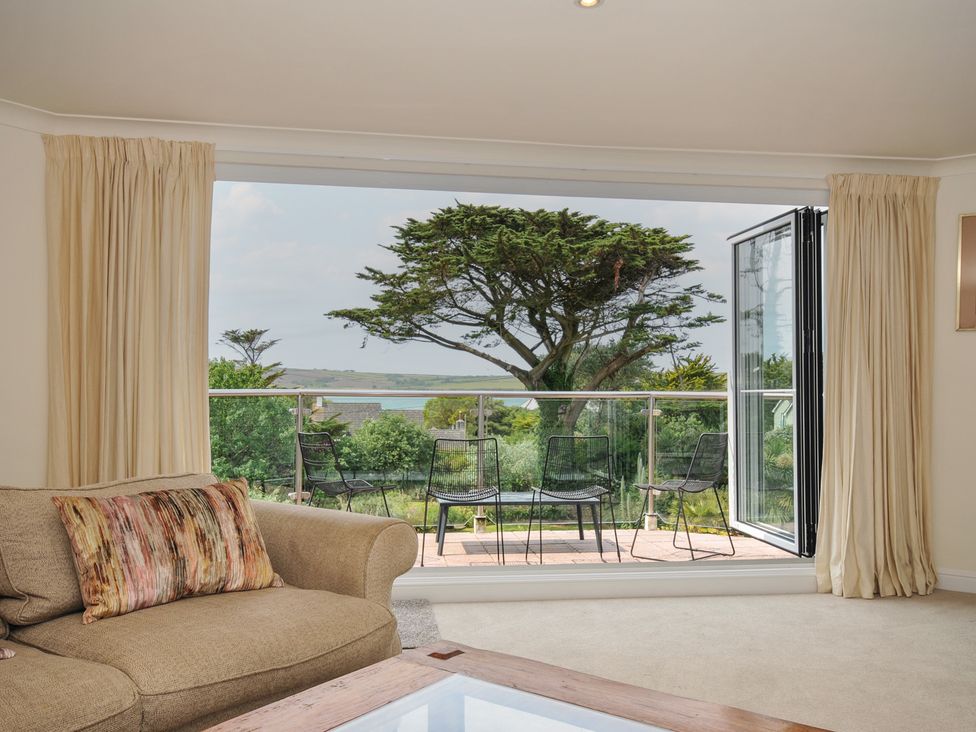 A living room with a sofa and glass door leading to outdoor seating at Bodare 8 Daymer Bay