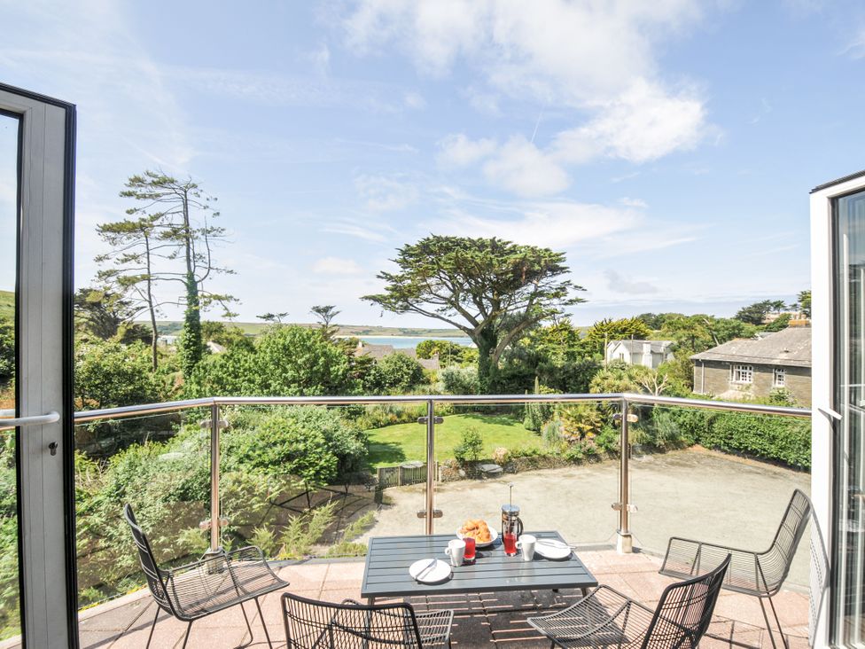 A balcony with a table and chairs overlooking a garden and water at Bodare 8 in Daymer Bay