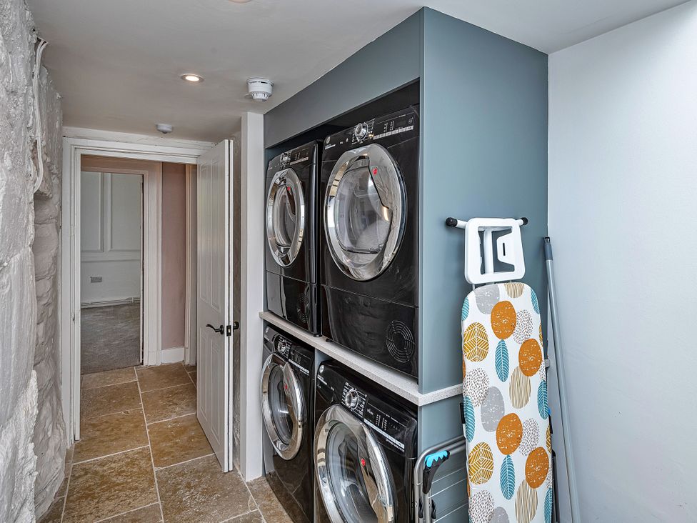A laundry room with stacked washer and dryer and an ironing board at Snowdonia Manor in Dolgellau