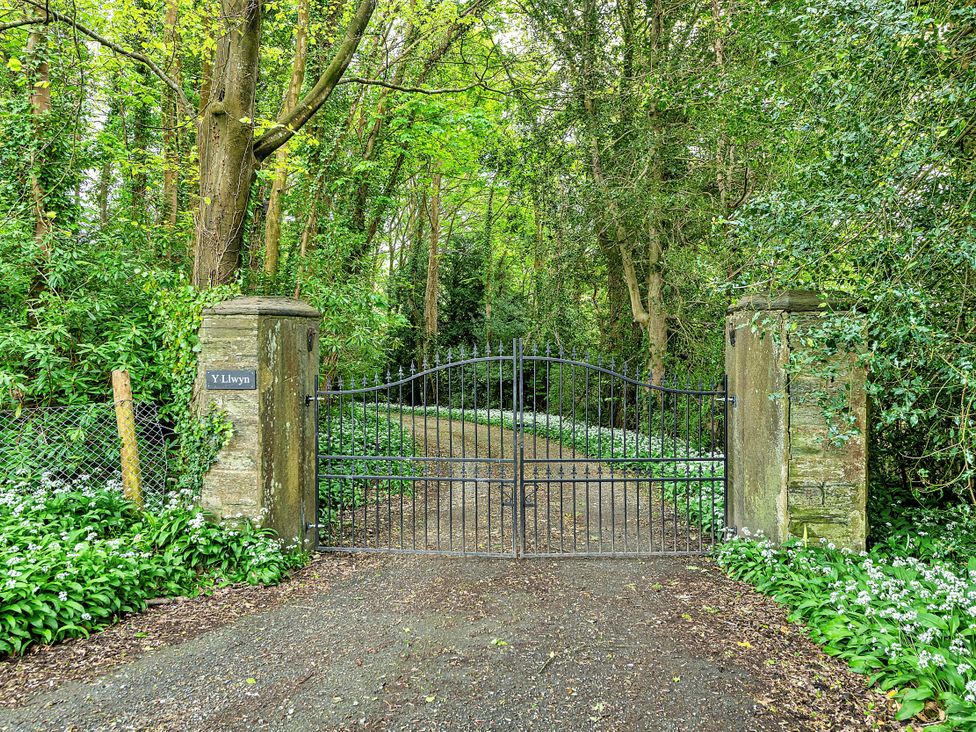 A gated entrance surrounded by trees and flowers at Y Llwyn in Dolgellau