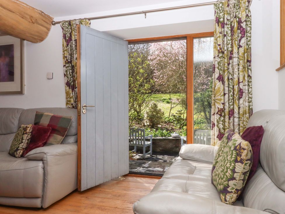A living room with a door and window opening to a garden at Swallows Reach Halwell