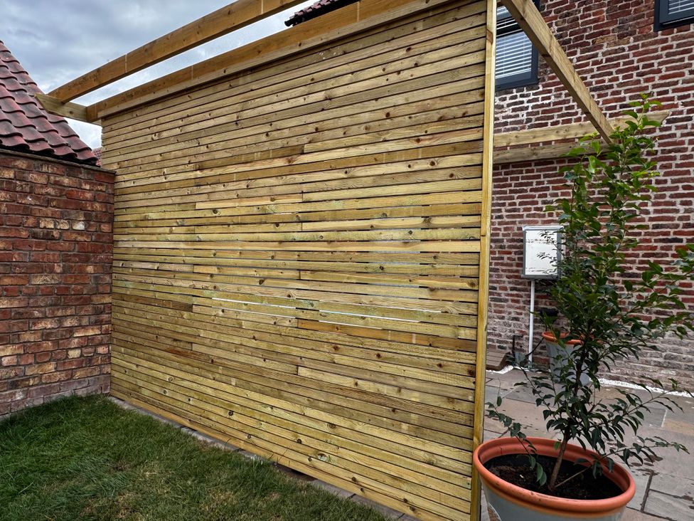 A wooden wall next to a brick wall with a plant in a pot at Courtenay House Harpham near Nafferton