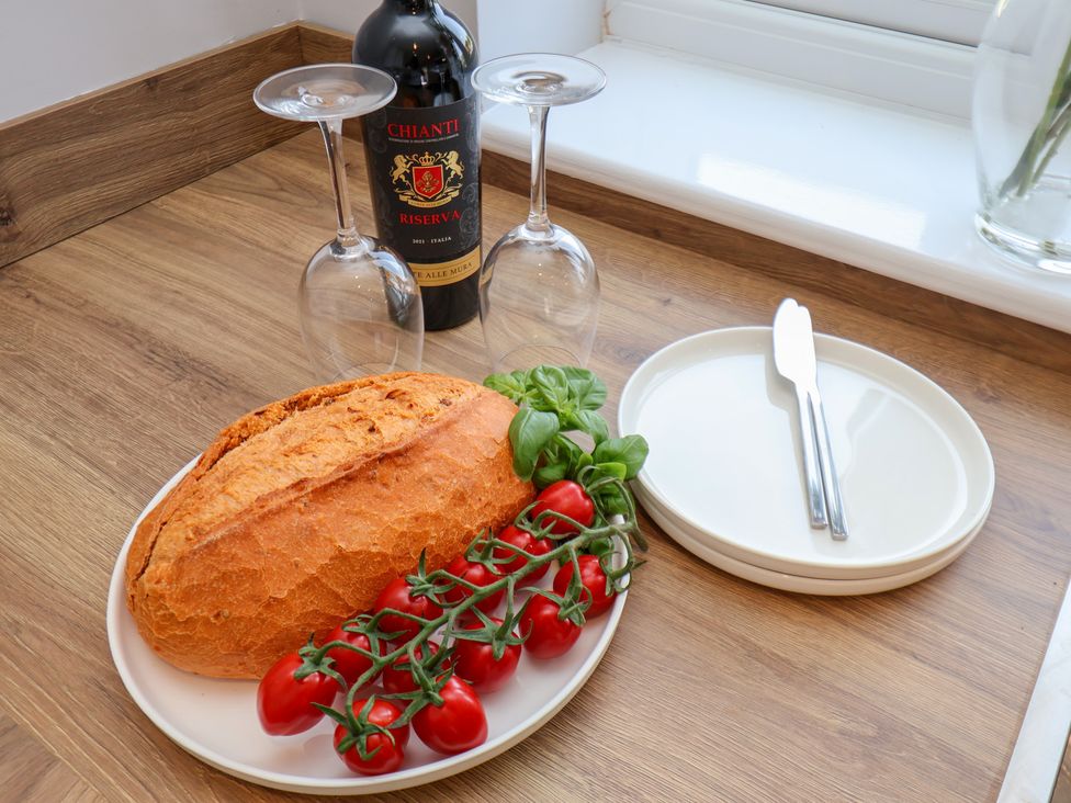 A kitchen counter with wine, glasses, bread, tomatoes, and plates at Manor Cottage Harpham near Nafferton