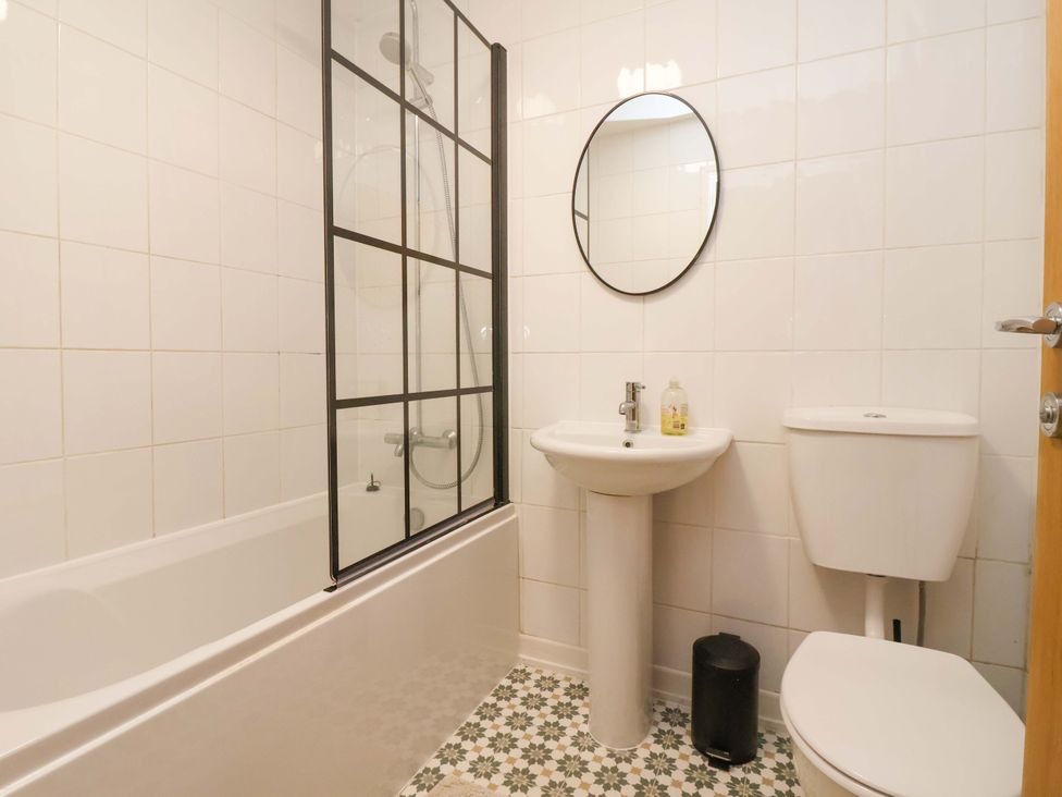 A bathroom with bathtub, shower, mirror, sink, and toilet at Apartment in Harrogate