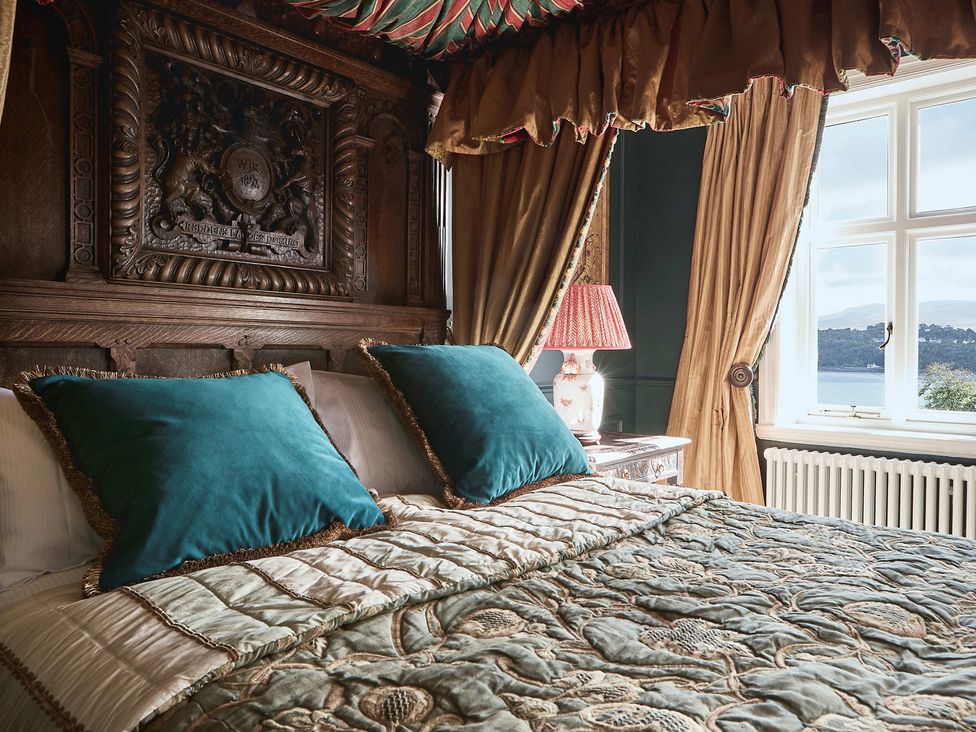 A bedroom with a detailed bed and window view at Craig y Don Glyngarth near Llandegfan