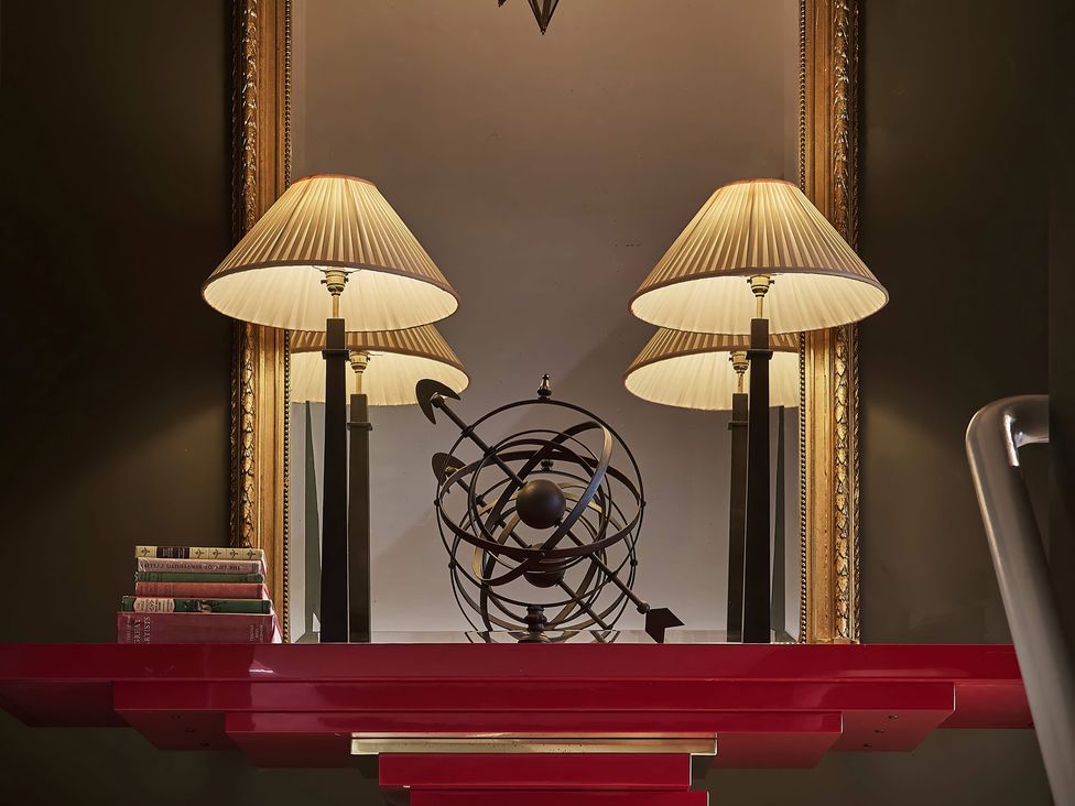 A living room with a red table, lamps, books, and a globe at Craig y Don in Glyngarth near Llandegfan