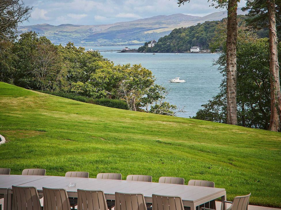 A garden with a table and chairs overlooking a body of water at Craig y Don Glyngarth near Llandegfan