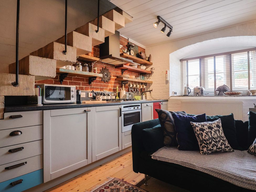 A kitchen with a microwave, oven, sink, sofa, and shelves at The Clock Tower in Rousdon, Nr Lyme Regis