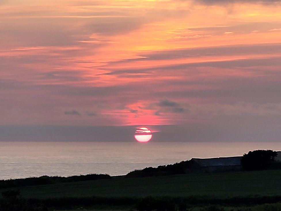 A sunset over the ocean with a silhouette of land at Badgers Sett Stibb near Kilkhampton