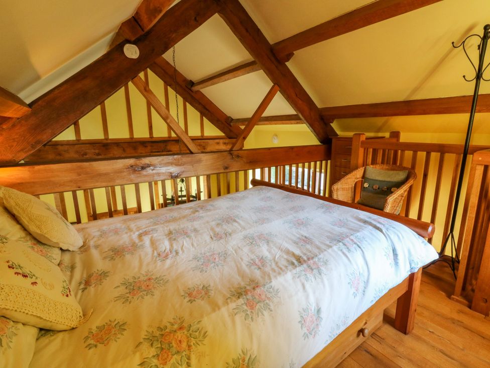 A loft with a bed and chair at Maggie's Barn in Brecon