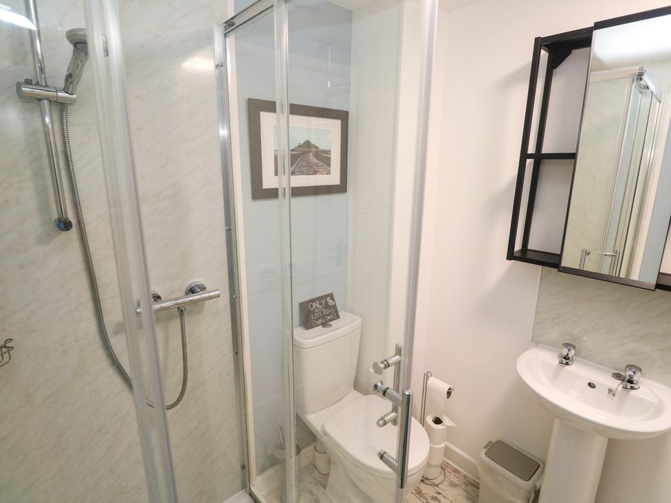 A bathroom with shower, toilet, sink, and storage shelf at The Packing House in Rosudgeon