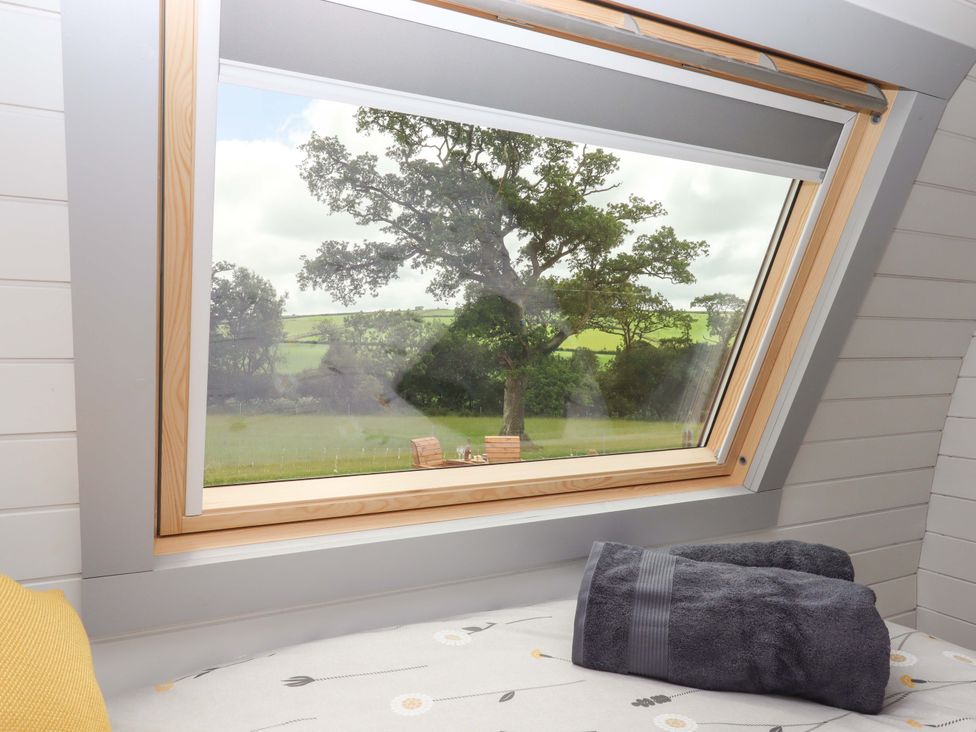 A bedroom window overlooking trees and countryside at Under Oak Pod in Totnes
