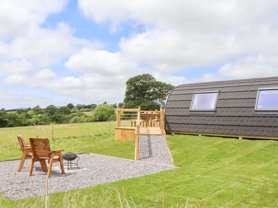 An outdoor space with wooden chairs and a fire pit at Under Oak Pod Totnes