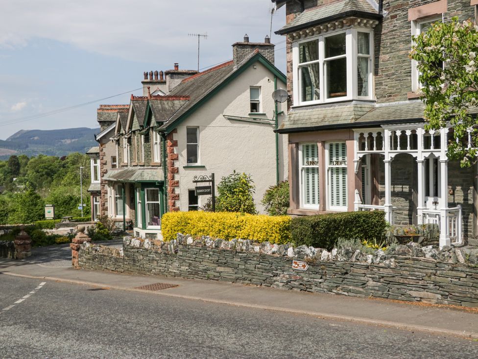 A row of stone and brick houses with a hedge and stone wall along a roadside at Sunnycroft in Keswick