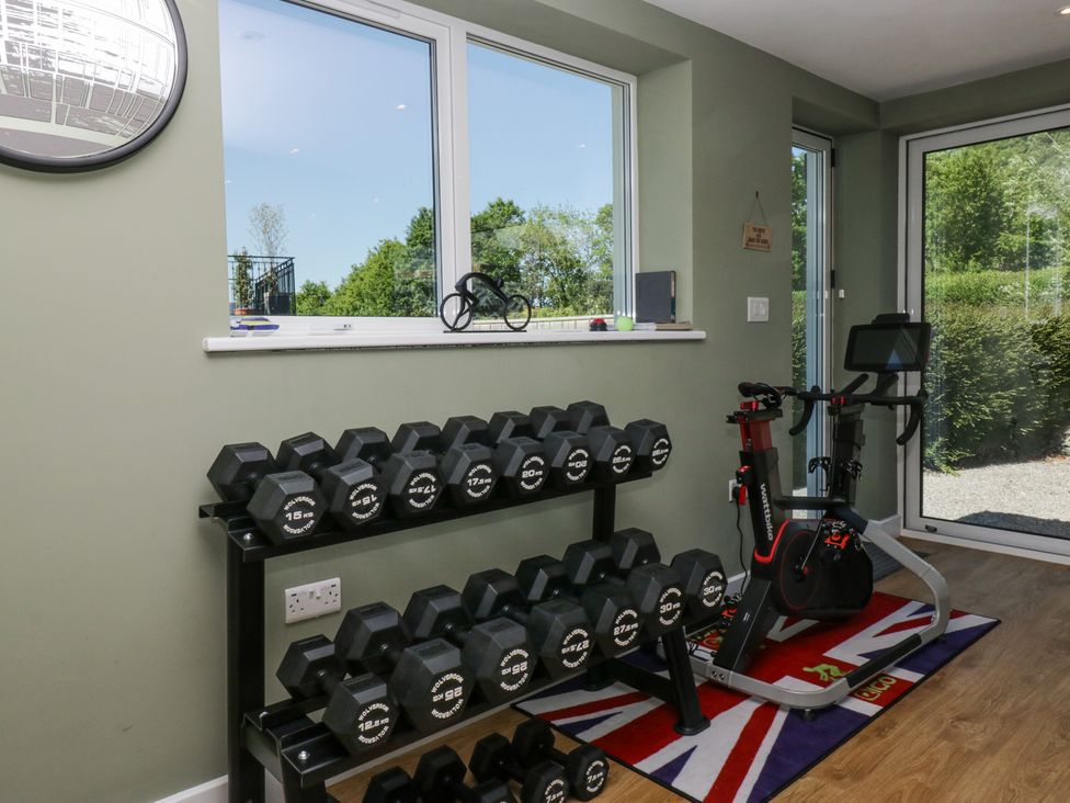 A home gym with dumbbell rack and stationary bike near large windows at Sunnycroft in Keswick