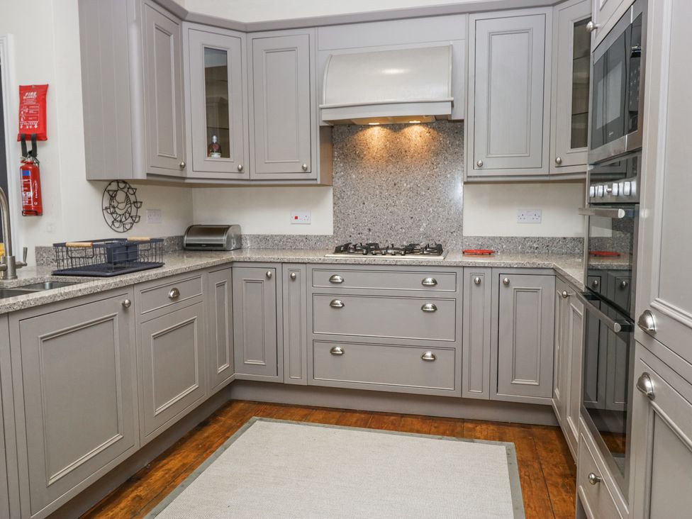 A kitchen with grey cabinets a gas stove a bread box a dish rack and a built-in oven at Sunnycroft in Keswick