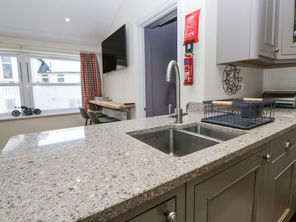 A kitchen countertop with a double sink and faucet with seating area and television on the wall at Sunnycroft in Keswick