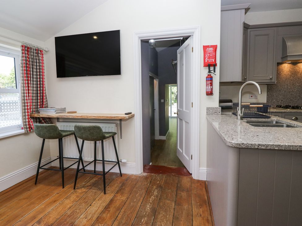 A kitchen area with two bar stools at a counter under a wall-mounted TV and an open door showing a hallway at Sunnycroft in Keswick