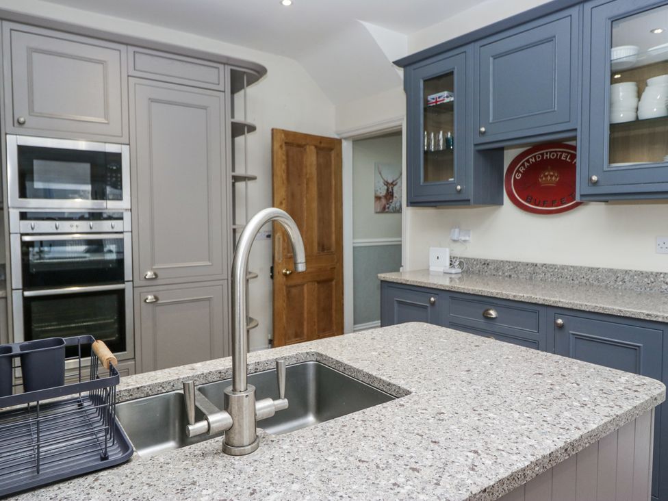 A kitchen with a double sink and faucet on a stone countertop with built in ovens and blue and gray cabinets at Sunnycroft in Keswick