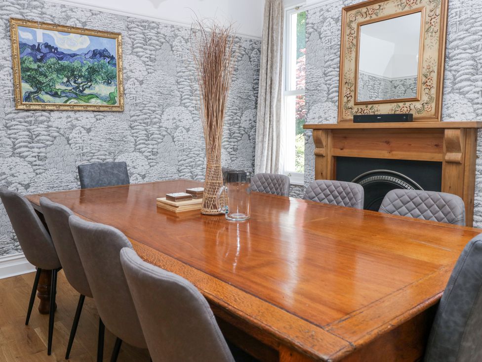 A dining room with a wooden table surrounded by gray chairs a fireplace with a mirror above and a painting on the wall at Sunnycroft in Keswick