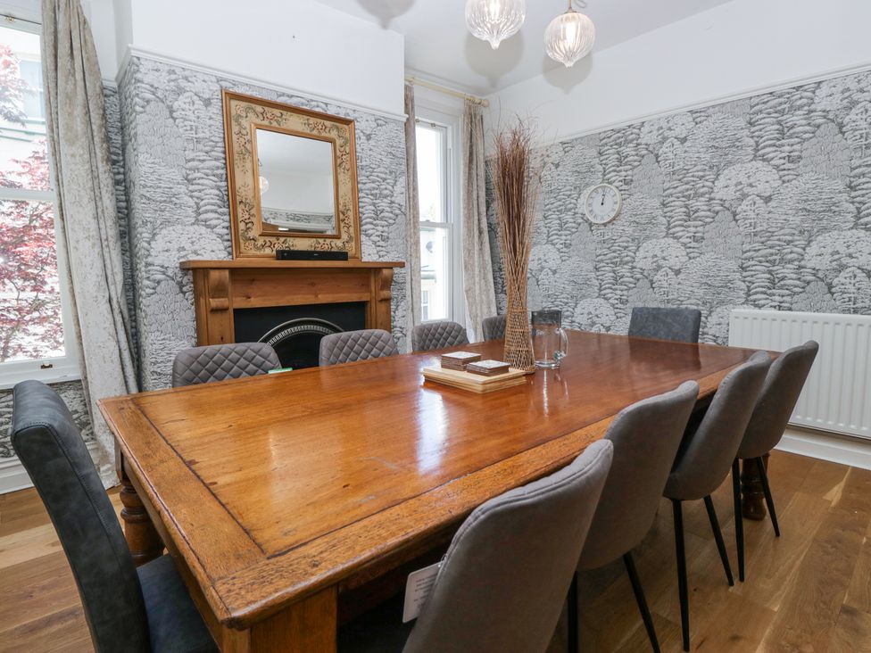 A dining room with a wooden table and upholstered chairs near windows and a fireplace at Sunnycroft in Keswick