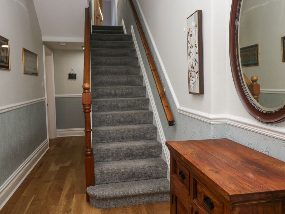 A staircase with carpet and wooden handrail next to a wooden cabinet with a round mirror above in a hallway at Sunnycroft in Keswick