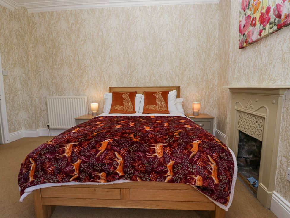 A bedroom with a wooden bed covered by a blanket with fox patterns two pillows with fox images two bedside tables with lamps and a fireplace at Sunnycroft in Keswick