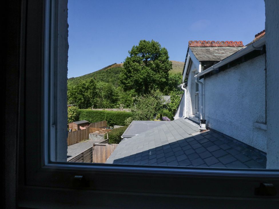 A view from a window showing rooftops trees a hill and a fenced garden at Sunnycroft Keswick
