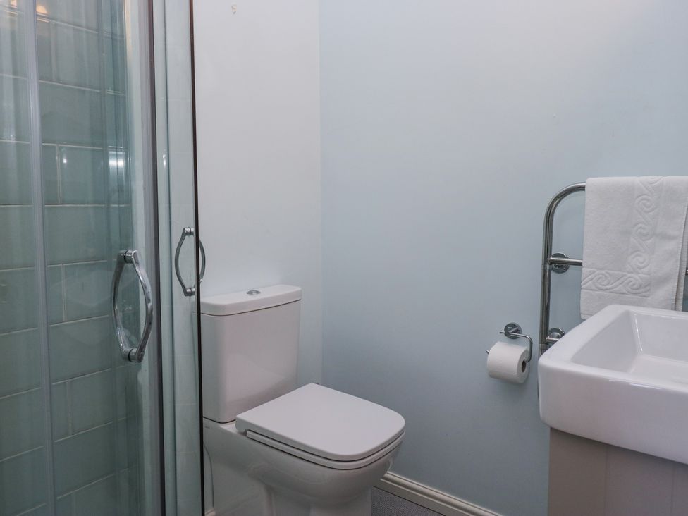 A bathroom with a toilet next to a glass shower enclosure and a sink with a towel rail at Sunnycroft in Keswick