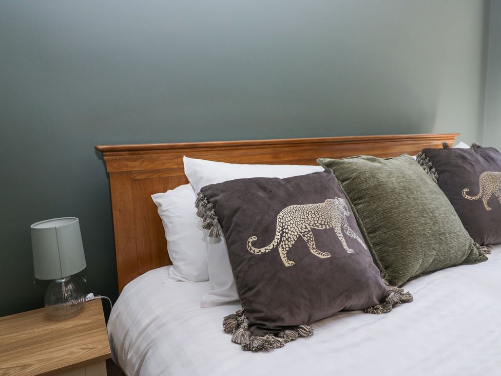 A bed with wooden headboard and decorative pillows with animal designs and fringes beside a bedside table with a lamp