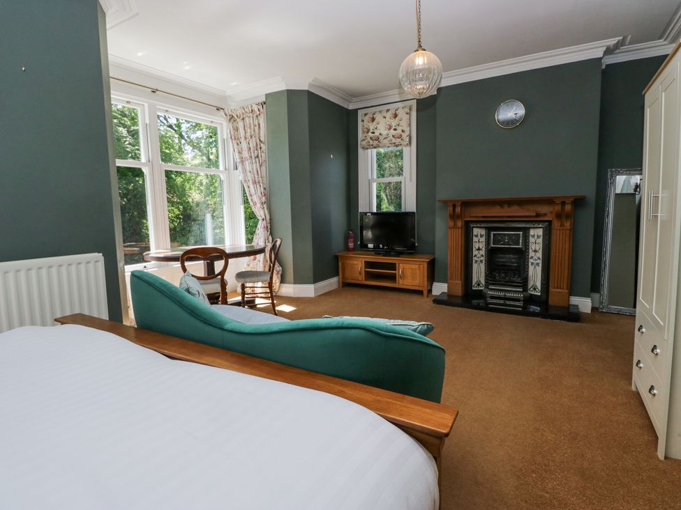A bedroom with a bed sofa table chairs fireplace and wardrobe at Sunnycroft in Keswick