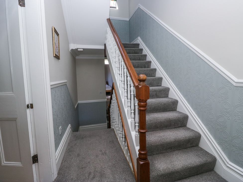 A carpeted staircase with wooden handrail and white balusters in a hallway with half-height patterned blue walls and a small framed picture at Sunnycroft in Keswick