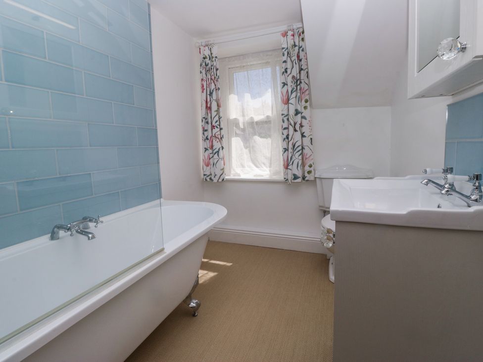 A bathroom with a bathtub sink and window with floral curtains at Sunnycroft in Keswick