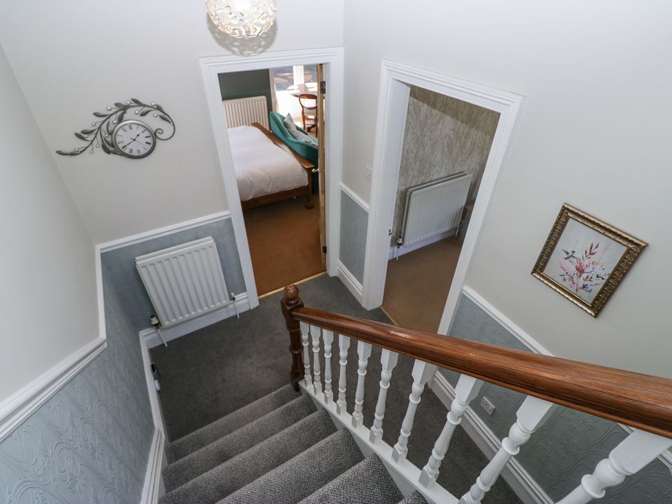 A staircase with a wooden handrail and white spindles leading to a landing with two doorways a wall clock and a framed picture on the walls at Sunnycroft in Keswick