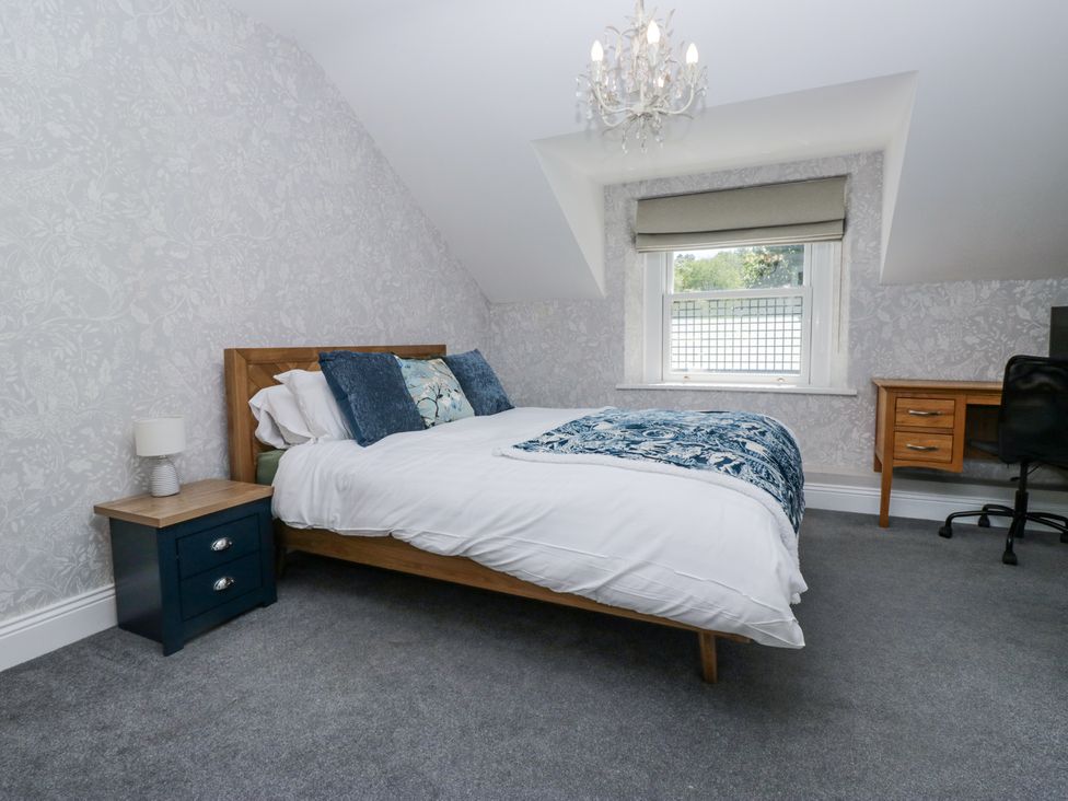 A bedroom with a bed with pillows and a blanket a bedside table with a lamp a window a desk and a chair at Sunnycroft Keswick