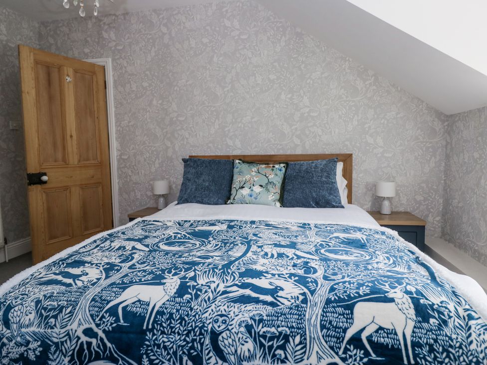 A bedroom with a wooden door a bed with blue and white animal patterned blanket and decorative pillows at Sunnycroft in Keswick