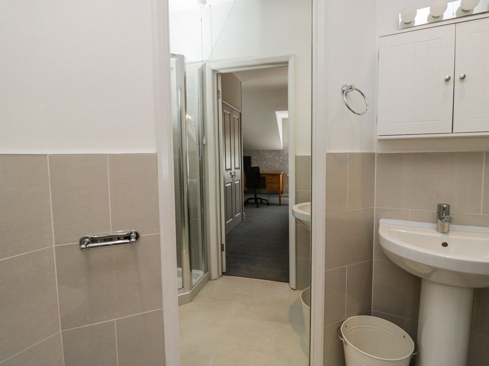 A bathroom with a pedestal sink and cabinet next to a shower room leading to a carpeted office with a desk and chair at Sunnycroft in Keswick