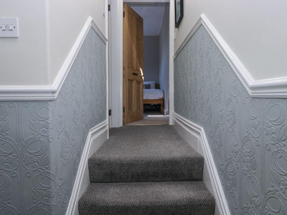 A carpeted staircase with decorative wall panels leading to a room with an open wooden door and a bed visible at Sunnycroft in Keswick