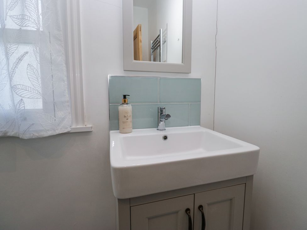 A bathroom sink with a soap dispenser a mirror above and a window with a sheer curtain at Sunnycroft in Keswick