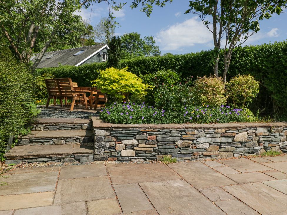 A garden patio with stone steps and wall leading to wooden chairs and table surrounded by plants and flowers at Sunnycroft in Keswick