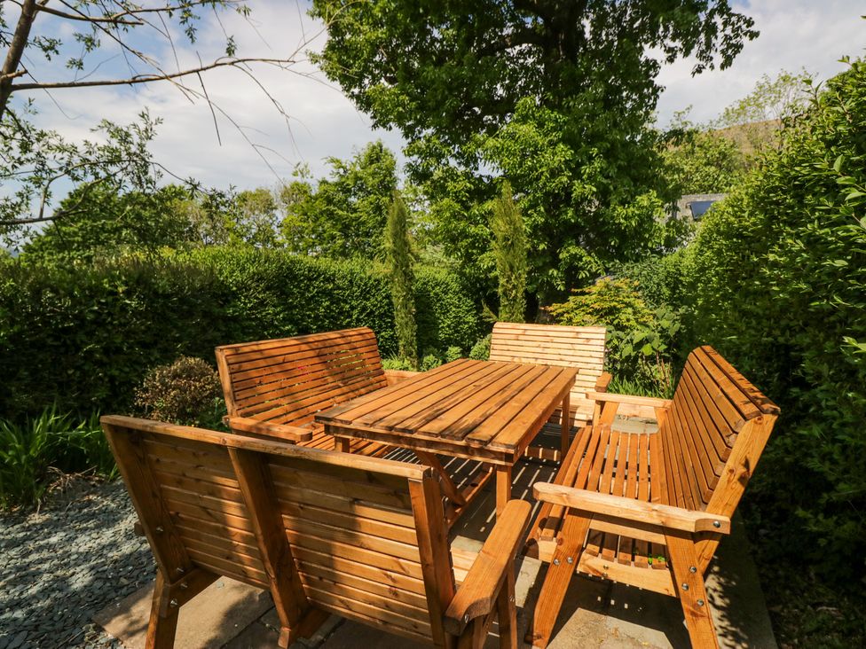 An outdoor wooden table with four matching benches in a garden surrounded by trees and shrubs at Sunnycroft in Keswick