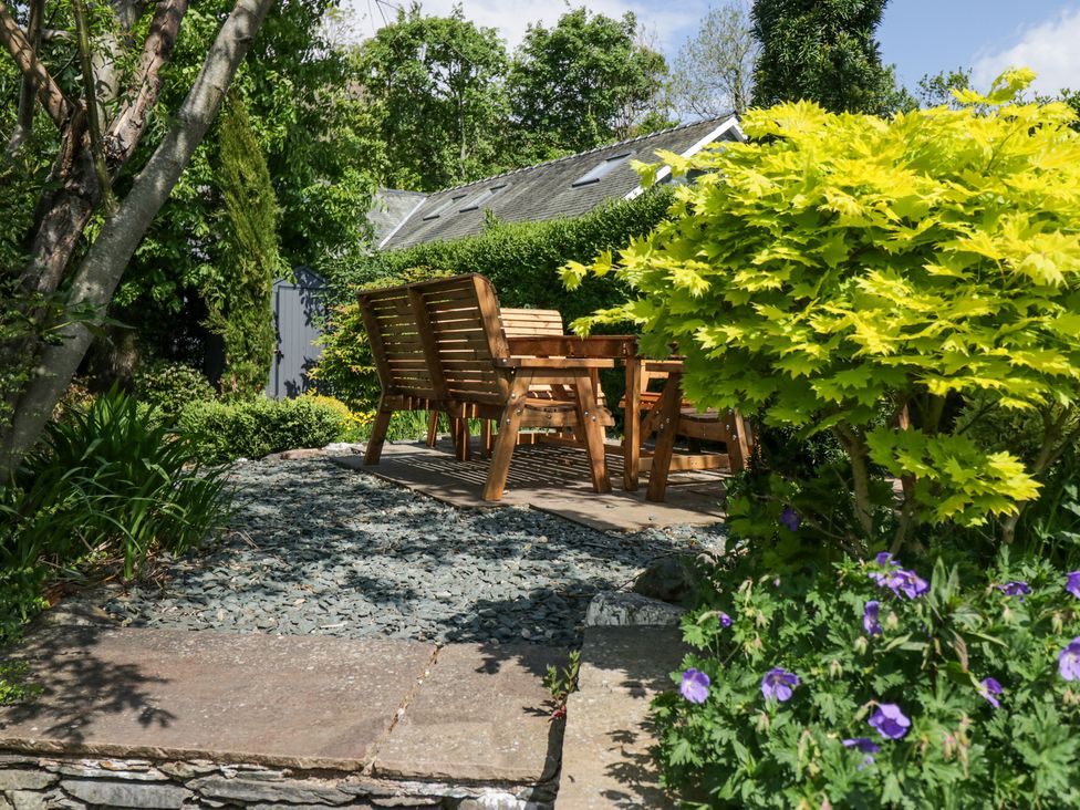 An outdoor seating area with wooden chairs and table surrounded by trees and plants at Sunnycroft in Keswick