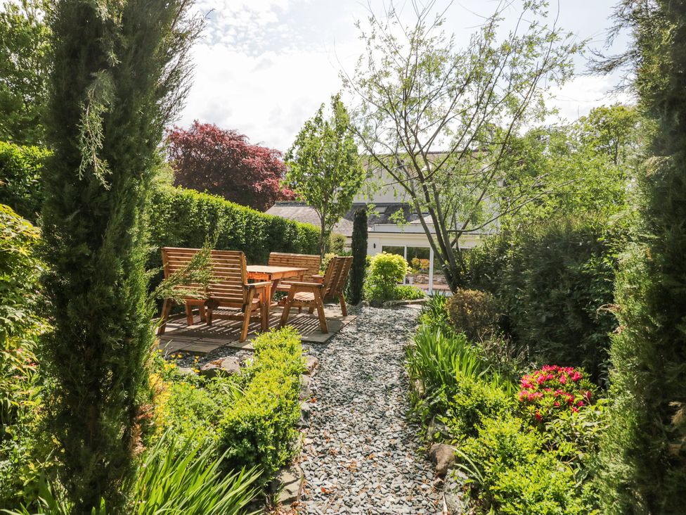 A garden with a gravel path leading to wooden outdoor furniture surrounded by green plants and trees at Sunnycroft in Keswick