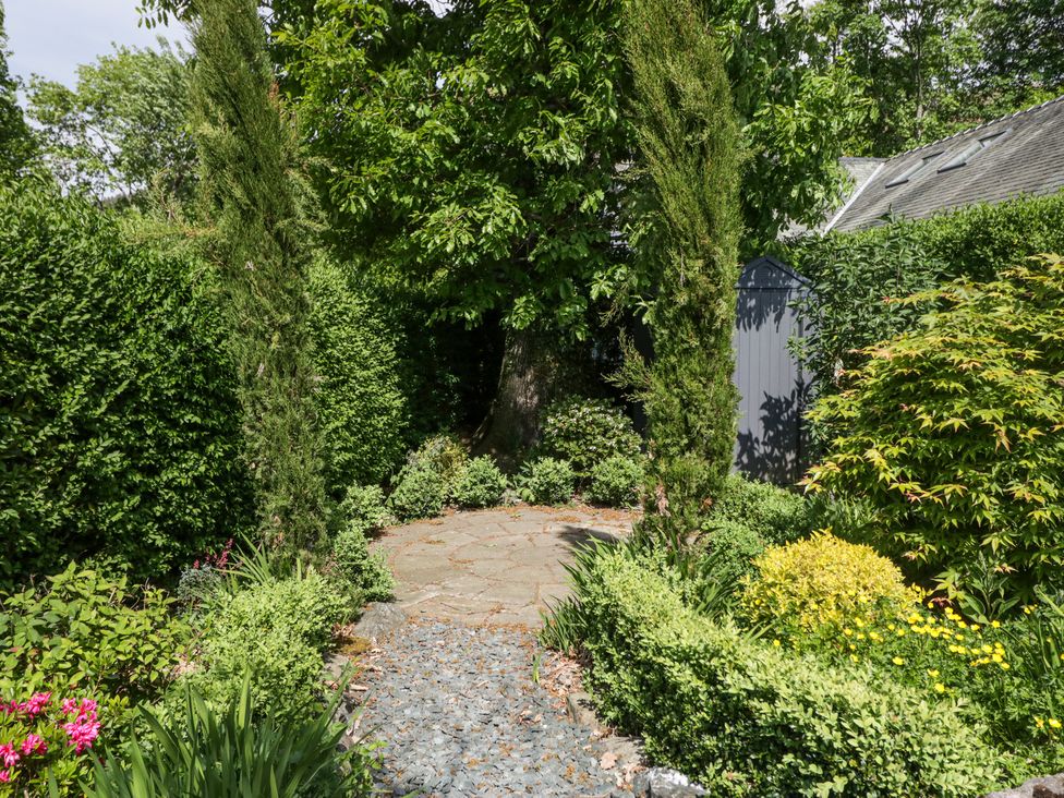 A garden path with gravel and stone surrounded by green shrubs and trees with a gray shed in the background at Sunnycroft in Keswick