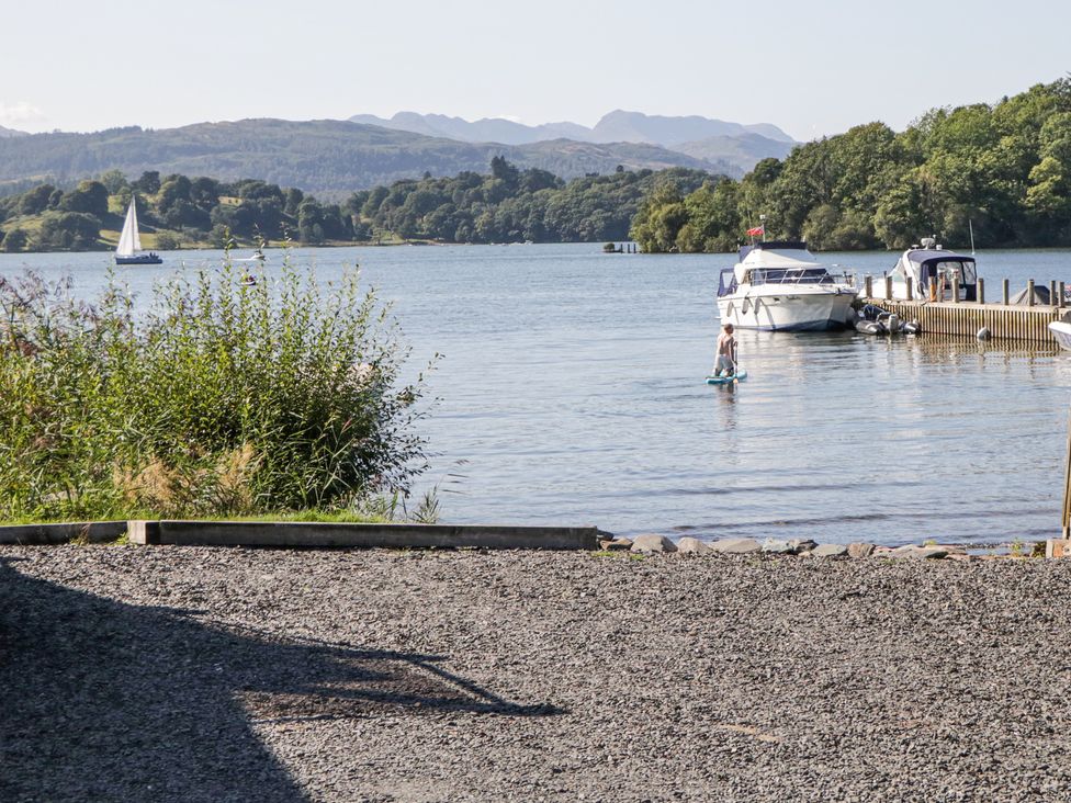 A lakeside scene with boats docked at a pier and a person paddleboarding on the water at Sunnycroft in Keswick