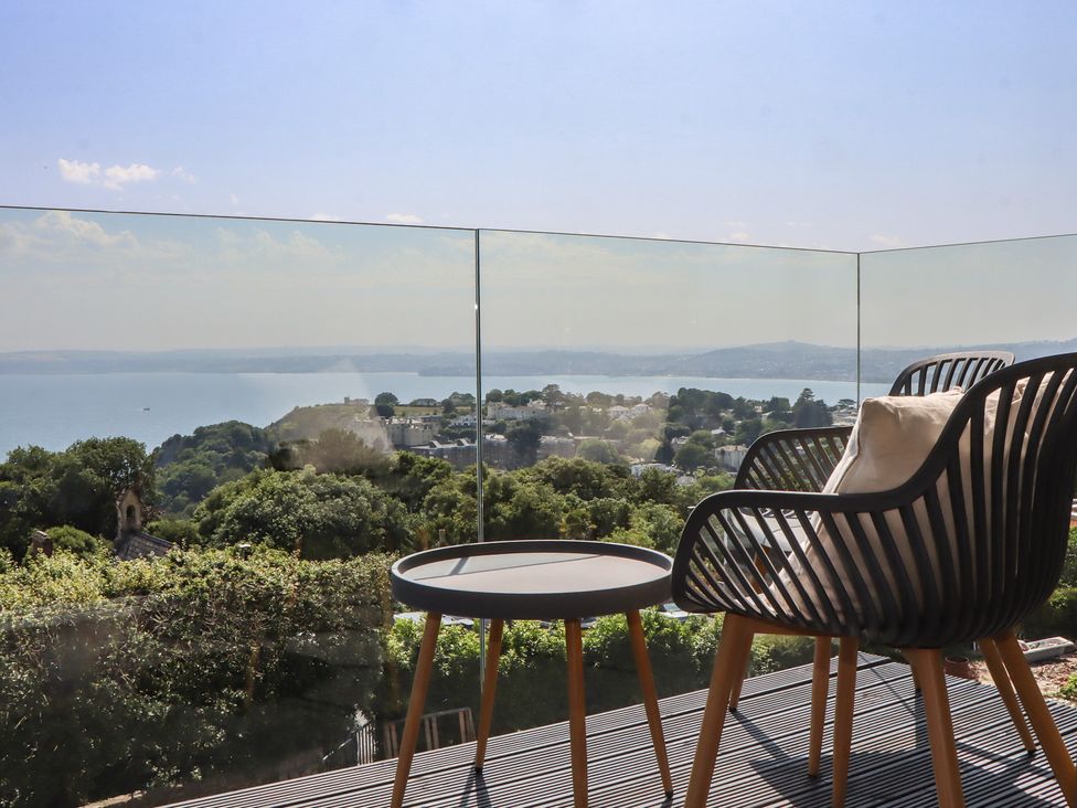 An outdoor balcony with a chair and table overlooking a coastal view at Seacroft in Torquay