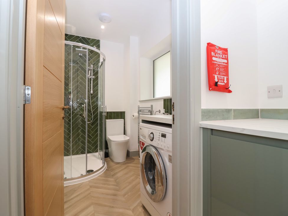 A bathroom with a shower, toilet, washing machine, and fire blanket at Seacroft in Wellswood near Torquay