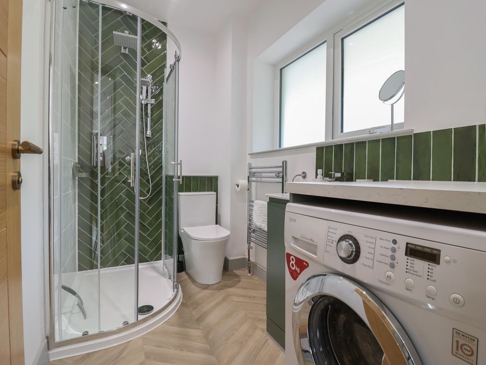 A bathroom with a shower, toilet, washing machine, and sink at Seacroft in Wellswood near Torquay